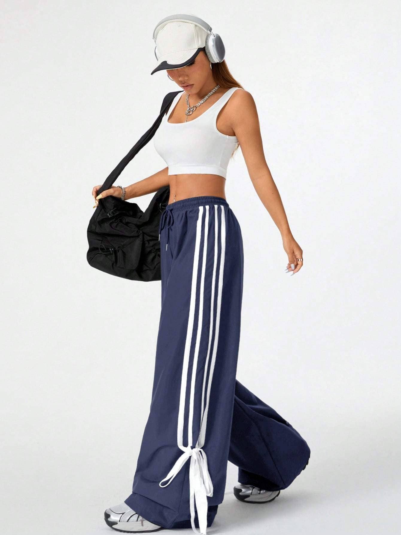 girl with white tank and navy athletic pants with white stripes down sides carrying a bag and wearing headphones